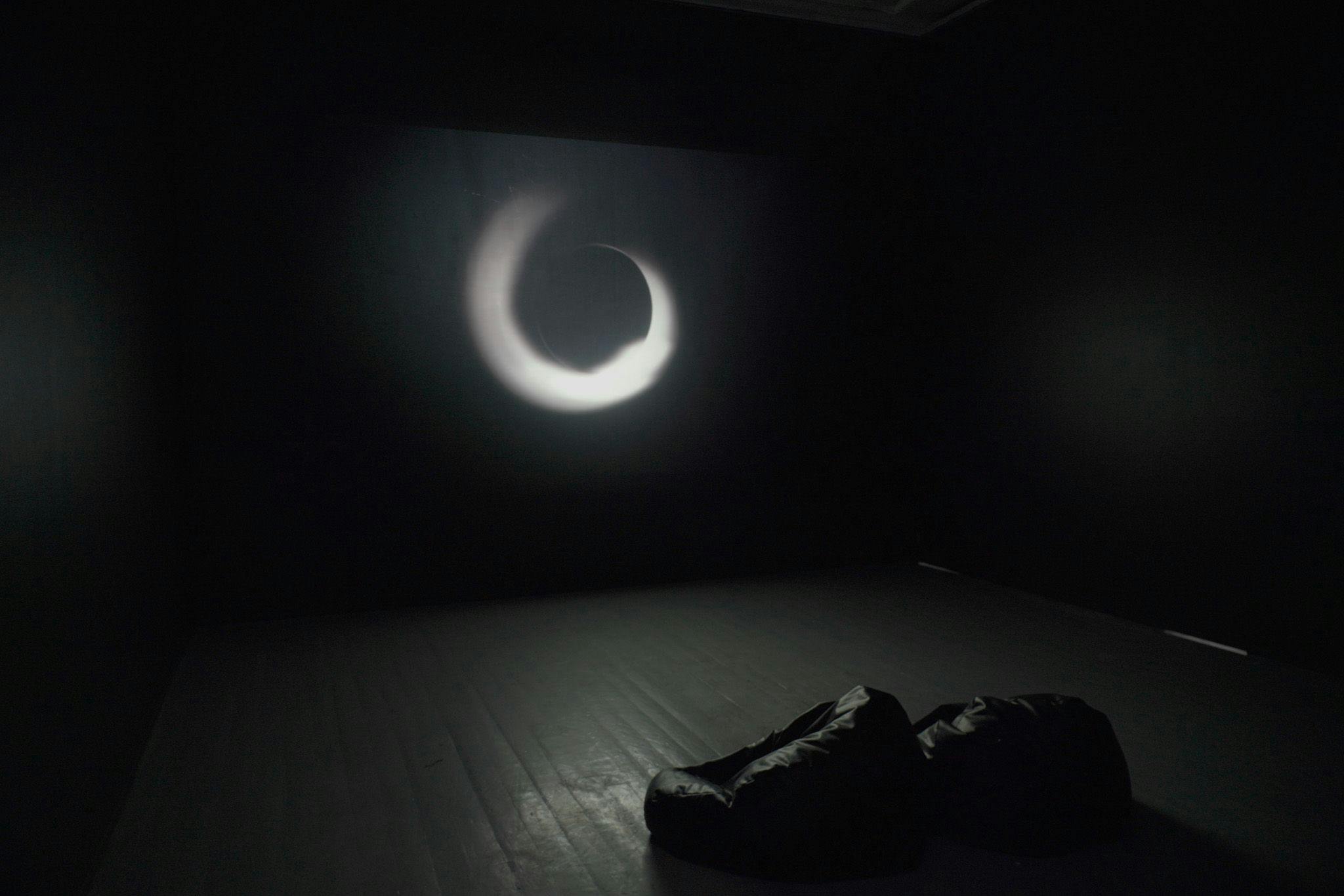 A swirl of light is projected in a black room with some black beanbags.