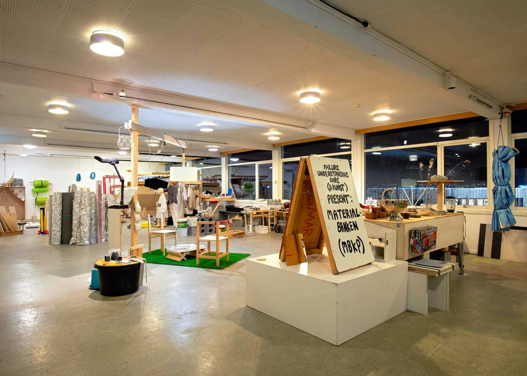 A large room filled with various objects. A poster board reads 'Material banken'.