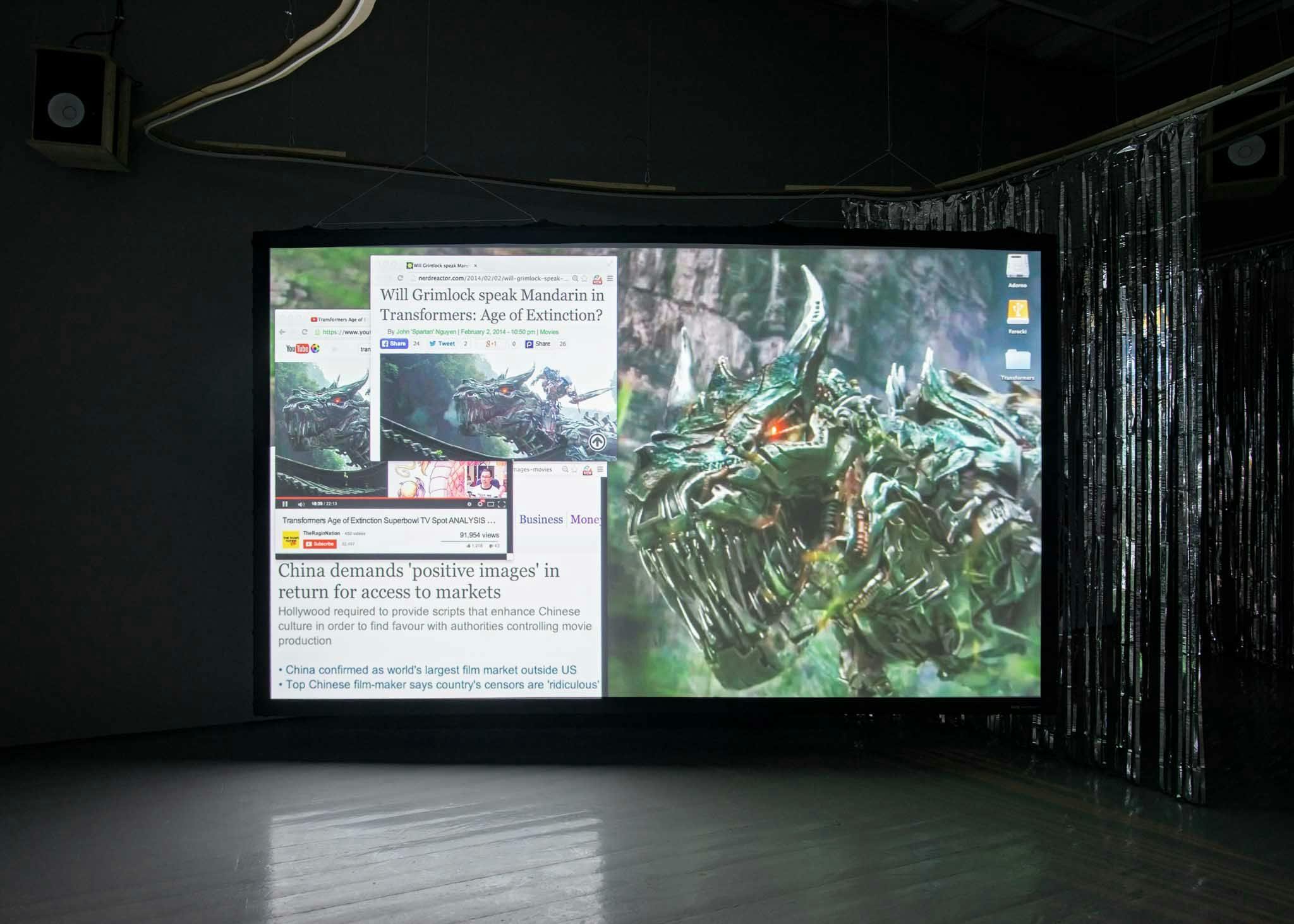 A bright projection screen in a gallery shows news clippings and a monster