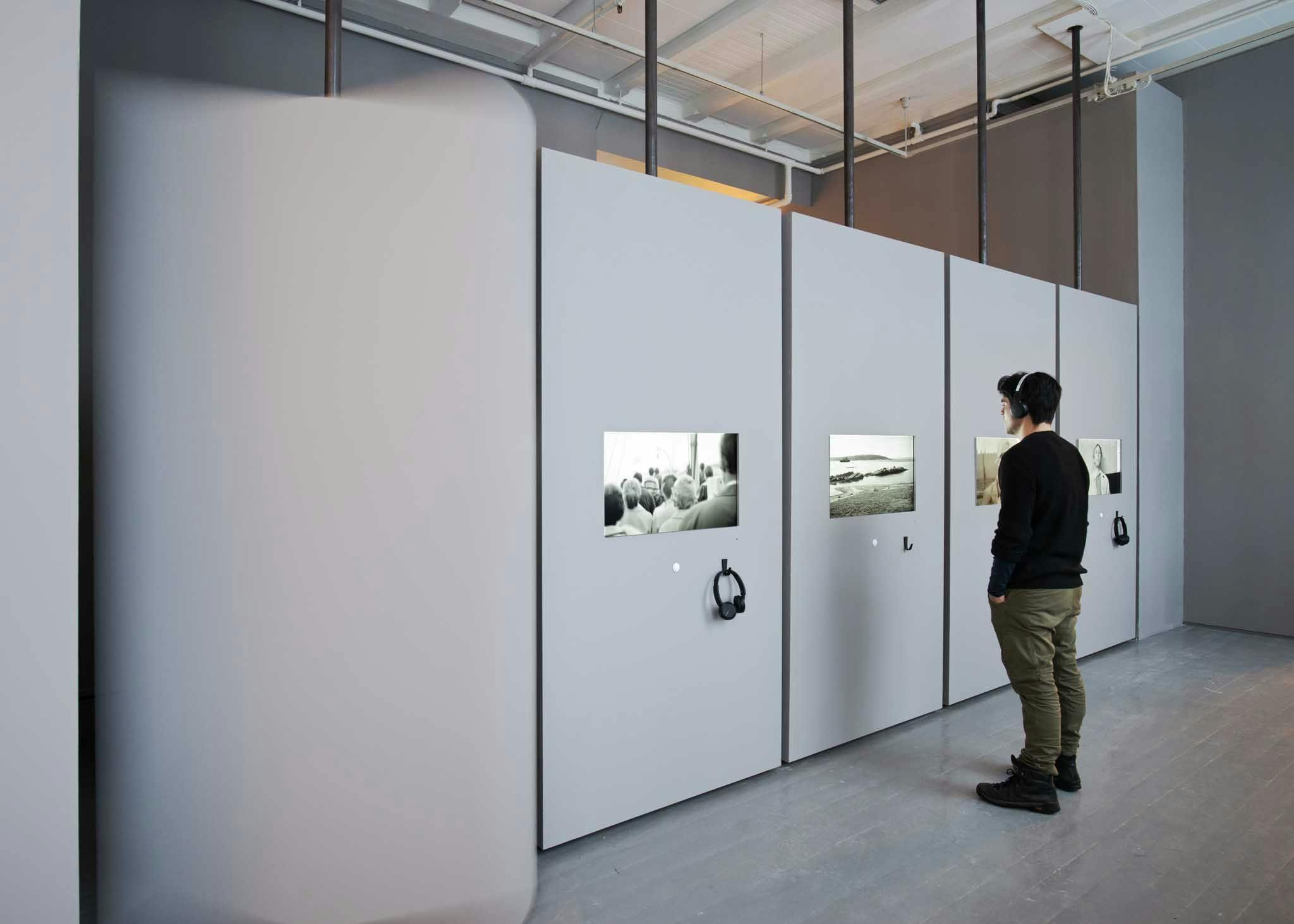 A man watches a black and white film in an installation, listening through headphones