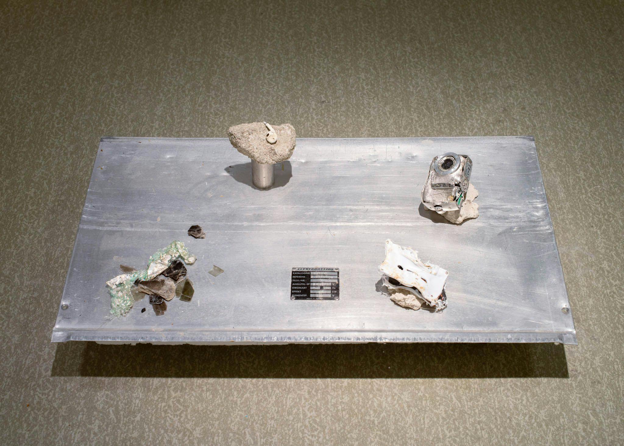 Various melted objects are displayed on an aluminium sheet.