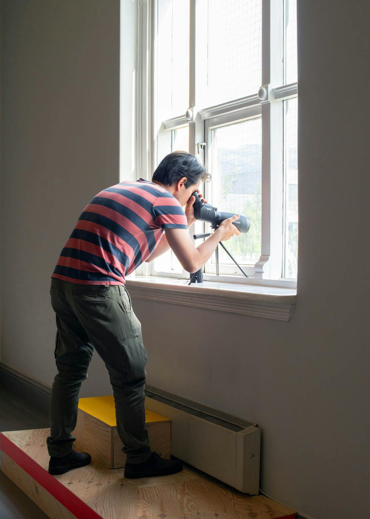A man looks through a telescope out of a window